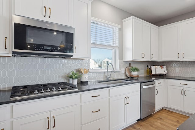 kitchen with white cabinetry, dark countertops, stainless steel appliances, light wood finished floors, and a sink