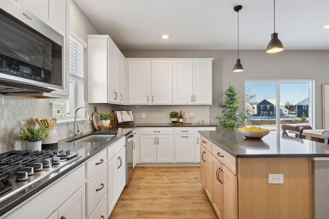 kitchen with a sink, light wood-style flooring, dark countertops, and stainless steel appliances