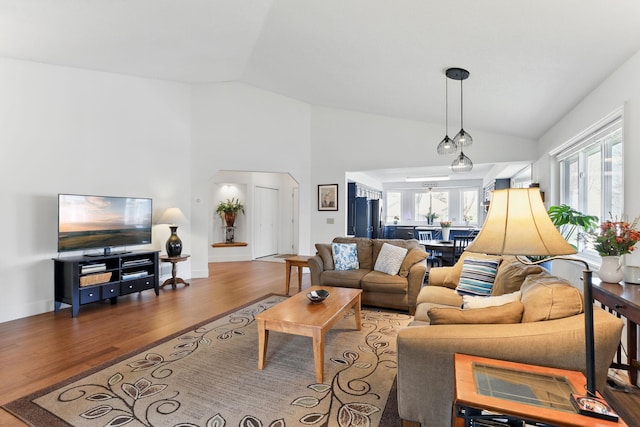 living room featuring arched walkways, wood finished floors, lofted ceiling, and baseboards