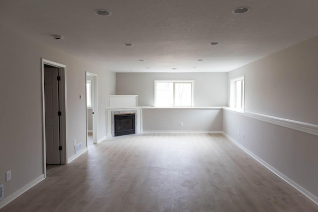 unfurnished living room featuring baseboards, wood finished floors, a high end fireplace, and visible vents