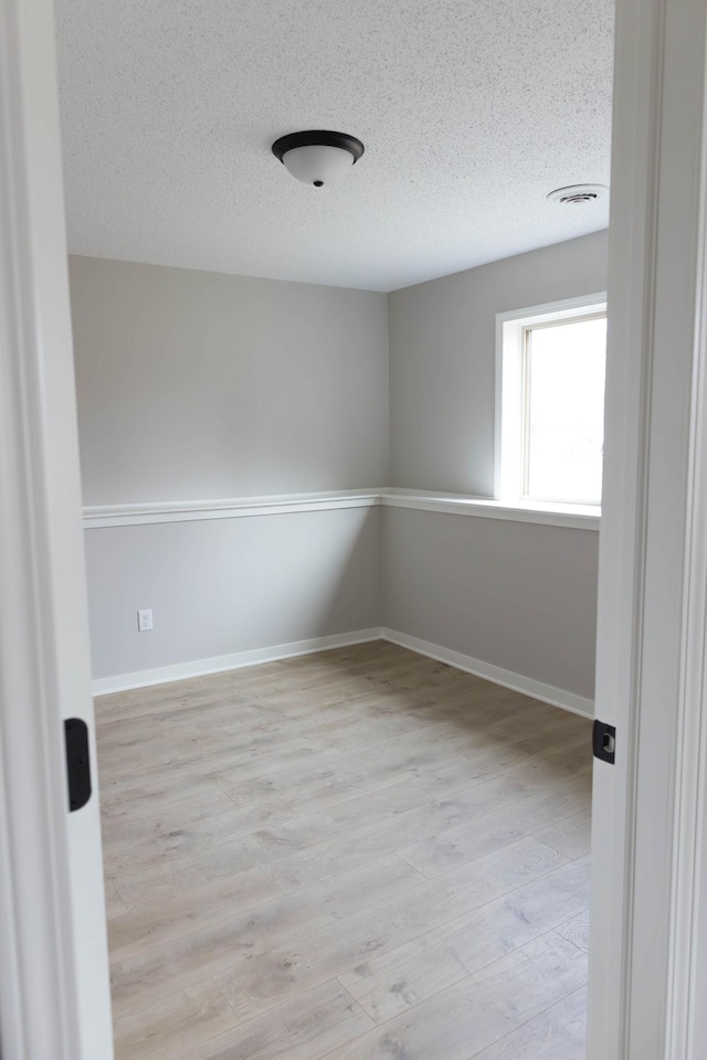empty room with a textured ceiling, baseboards, and light wood-type flooring