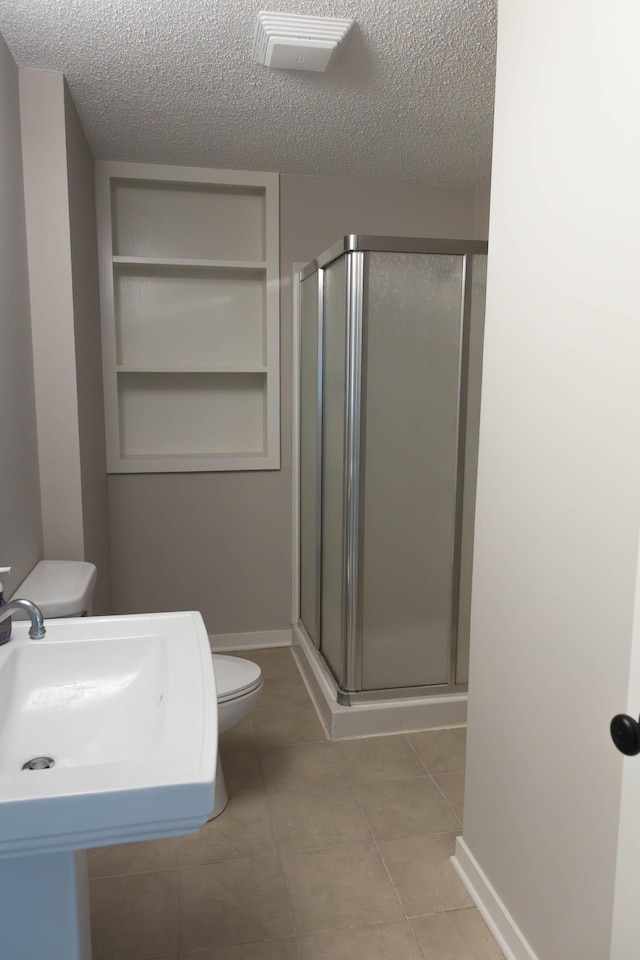 full bath featuring toilet, a textured ceiling, baseboards, and a stall shower