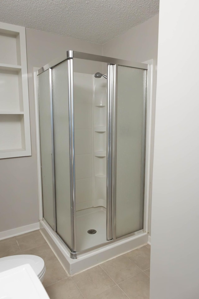 full bath with baseboards, a stall shower, tile patterned floors, a textured ceiling, and toilet