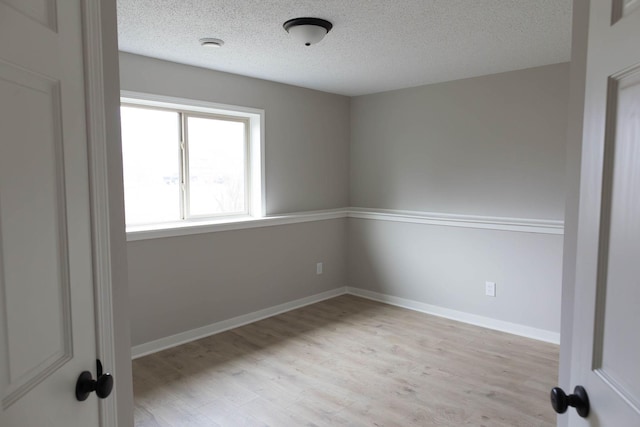 unfurnished room featuring baseboards, light wood finished floors, and a textured ceiling