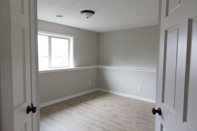 unfurnished room with a textured ceiling, baseboards, and light wood-style floors