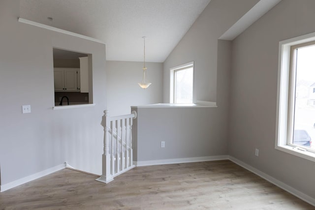 spare room featuring light wood-style flooring, baseboards, a sink, and lofted ceiling