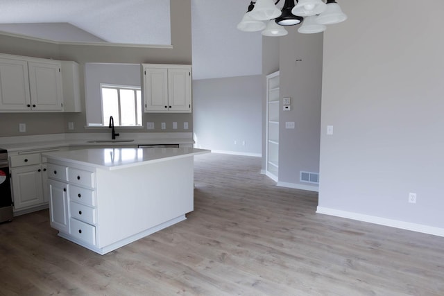 kitchen with white cabinets, visible vents, vaulted ceiling, and a sink