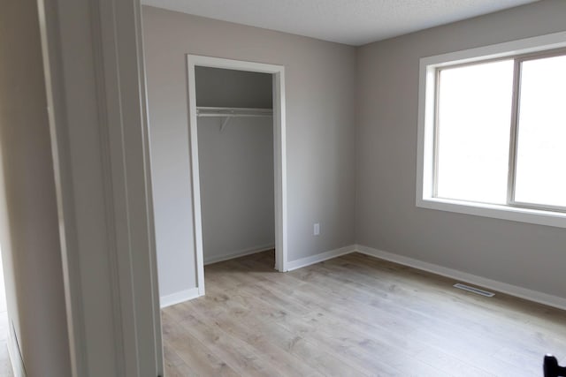 unfurnished bedroom with visible vents, light wood-style flooring, a closet, and baseboards
