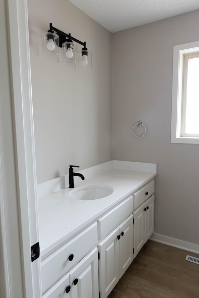 bathroom with vanity, visible vents, baseboards, and wood finished floors