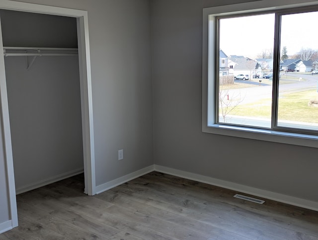 unfurnished bedroom with wood finished floors, multiple windows, and visible vents
