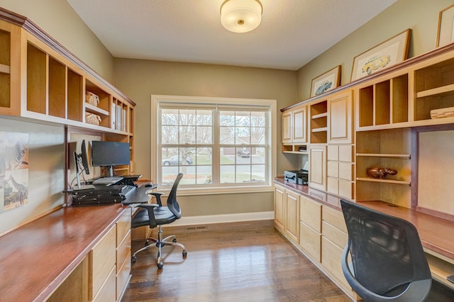 office area with visible vents, baseboards, dark wood finished floors, and built in study area