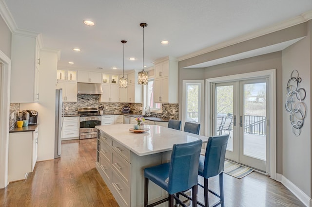 kitchen featuring a breakfast bar area, stainless steel appliances, decorative backsplash, under cabinet range hood, and dark wood-style floors