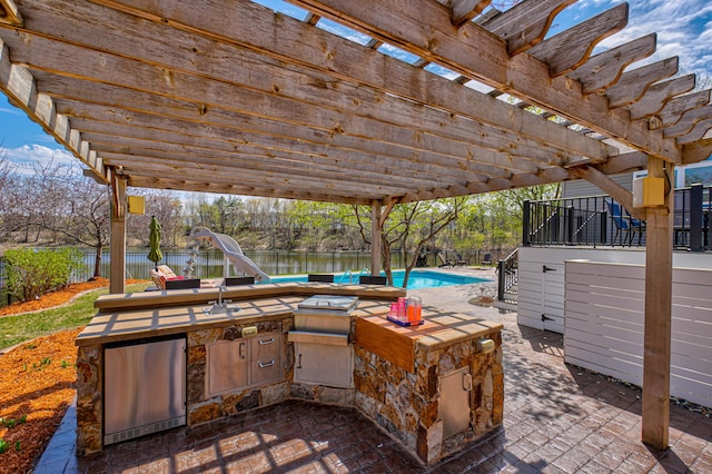 view of patio / terrace with fence, a pergola, an outdoor pool, an outdoor kitchen, and a water view