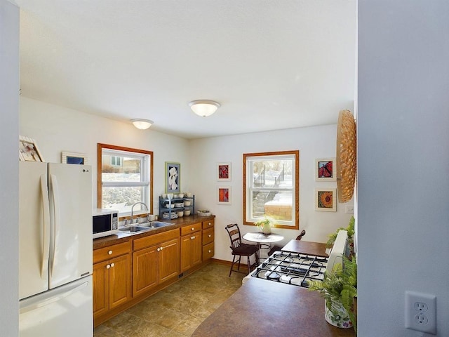 kitchen with brown cabinets, a sink, white appliances, and a wealth of natural light