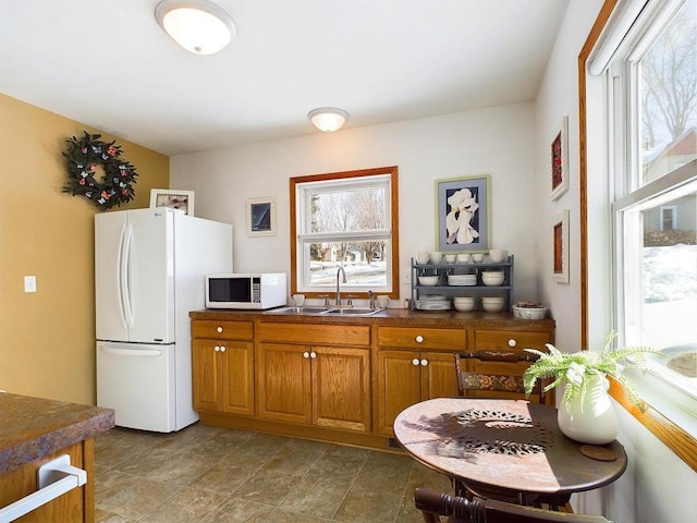 kitchen featuring brown cabinets, a wealth of natural light, white appliances, and a sink