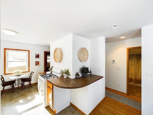 kitchen featuring dark countertops, white gas stove, baseboards, and recessed lighting