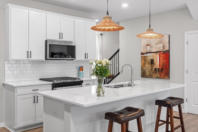 kitchen featuring tasteful backsplash, white cabinetry, light wood-style floors, stainless steel appliances, and a sink