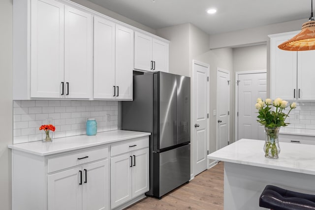 kitchen featuring tasteful backsplash, white cabinets, freestanding refrigerator, light wood-style floors, and pendant lighting