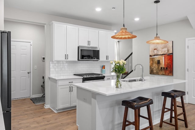 kitchen featuring white cabinets, a sink, appliances with stainless steel finishes, backsplash, and light wood-style flooring