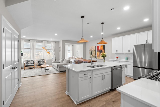 kitchen featuring a sink, light countertops, light wood-type flooring, stainless steel appliances, and decorative backsplash