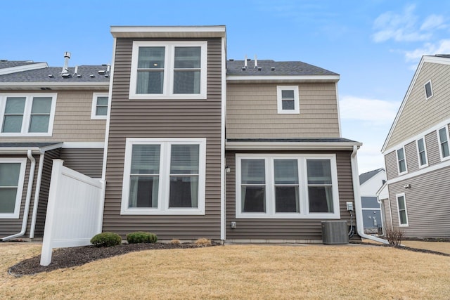 rear view of property featuring central AC unit, fence, and a lawn