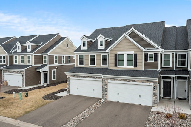 townhome / multi-family property featuring an attached garage, a shingled roof, stone siding, and driveway