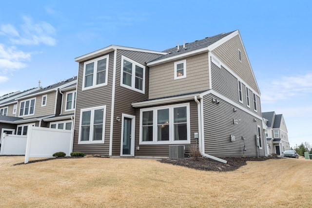 rear view of property featuring central AC, fence, and a lawn