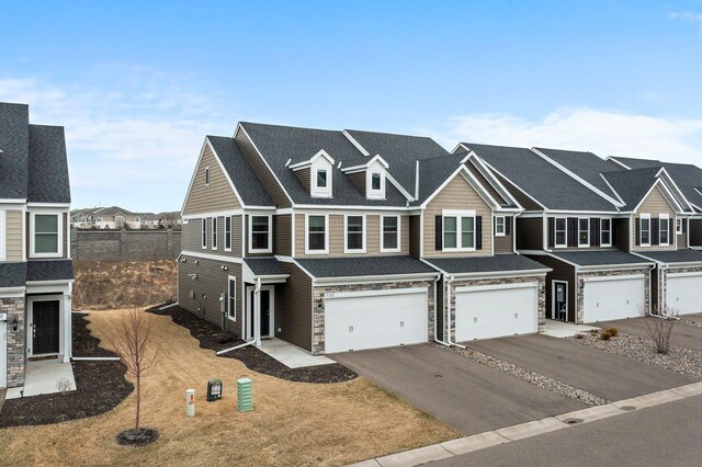 multi unit property featuring roof with shingles, stone siding, an attached garage, driveway, and a residential view