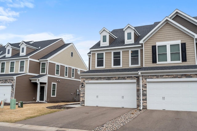 craftsman-style house featuring a shingled roof, stone siding, a garage, and aphalt driveway