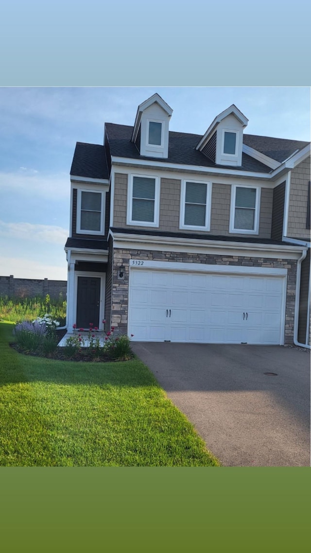 view of front facade featuring a front yard, stone siding, a garage, and aphalt driveway
