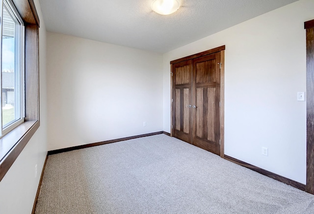 unfurnished bedroom with baseboards, carpet flooring, a closet, and multiple windows
