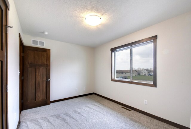 spare room featuring baseboards, carpet floors, visible vents, and a textured ceiling