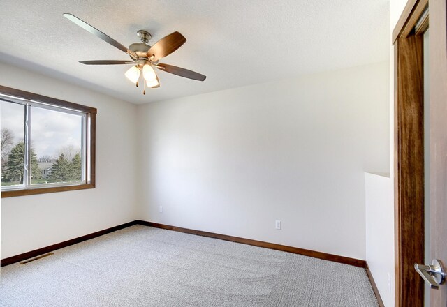 carpeted spare room featuring a textured ceiling, visible vents, a ceiling fan, and baseboards