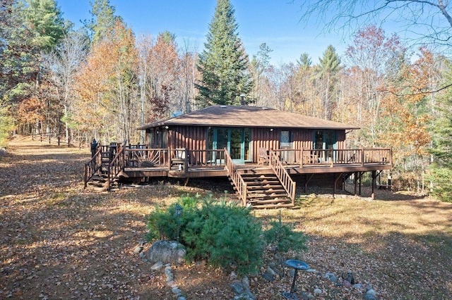 rear view of house featuring a view of trees, board and batten siding, a deck, and stairway