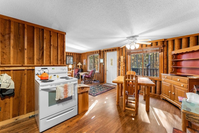 kitchen featuring white electric range oven, ceiling fan, wood finished floors, and wooden walls