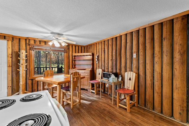 dining room with wood walls, a textured ceiling, wood finished floors, and ceiling fan