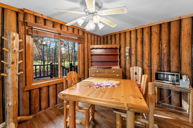 dining area with wood walls, a ceiling fan, wood finished floors, and a textured ceiling
