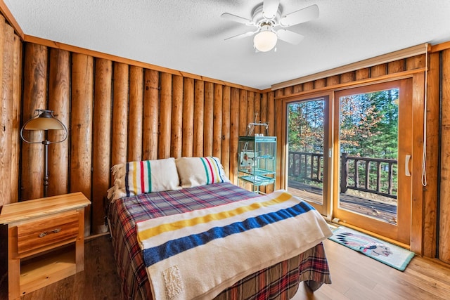 bedroom with a textured ceiling, access to exterior, wood finished floors, and wooden walls
