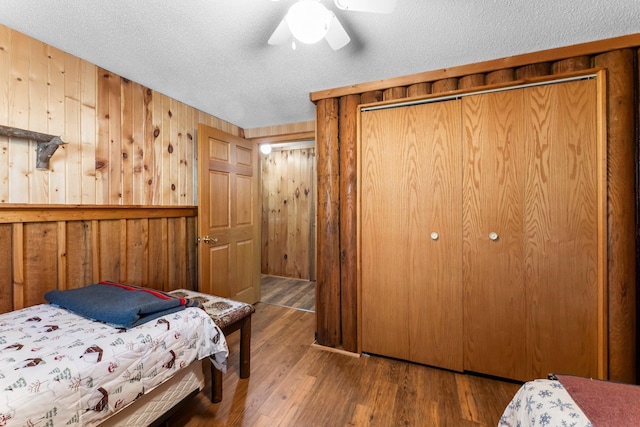 bedroom with a closet, wooden walls, a textured ceiling, and wood finished floors