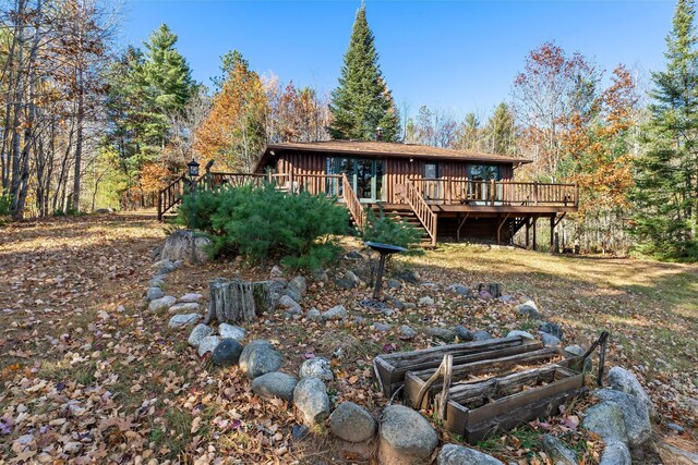 back of house featuring board and batten siding, a wooden deck, a garden, a forest view, and stairs