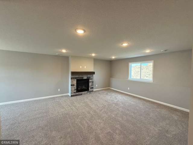 unfurnished living room featuring carpet flooring, baseboards, a stone fireplace, a textured ceiling, and recessed lighting