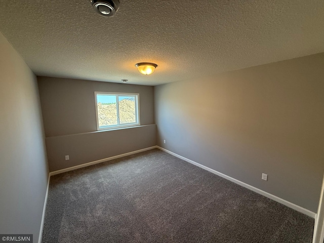 empty room with dark colored carpet, a textured ceiling, and baseboards