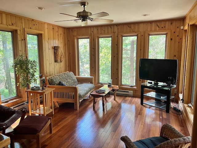 living area with baseboard heating, ornamental molding, wooden walls, ceiling fan, and wood-type flooring