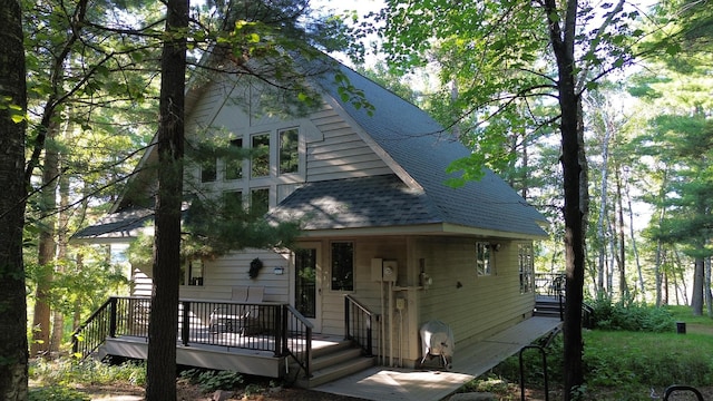 view of front facade featuring roof with shingles and a wooden deck