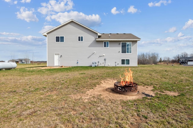 rear view of house with a yard, roof with shingles, and an outdoor fire pit
