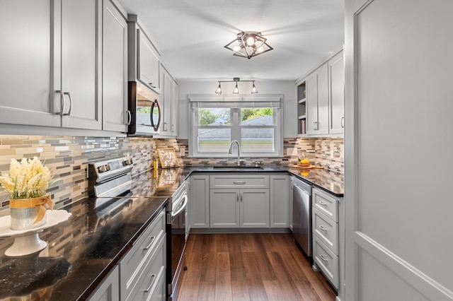 kitchen with appliances with stainless steel finishes, dark wood-style floors, a sink, tasteful backsplash, and dark stone counters
