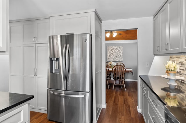 kitchen featuring stainless steel refrigerator with ice dispenser, dark countertops, dark wood finished floors, tasteful backsplash, and baseboards