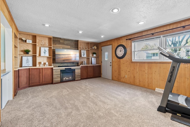 unfurnished living room with light colored carpet, wooden walls, a textured ceiling, a fireplace, and recessed lighting