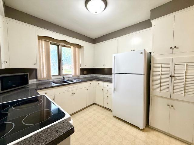 106 Mcphail Ave N, Caledonia, MN 55921 - kitchen with freestanding refrigerator, stainless steel microwave, dark countertops, white cabinetry, and light floors