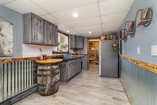 kitchen with light wood finished floors, a paneled ceiling, a sink, dark countertops, and freestanding refrigerator